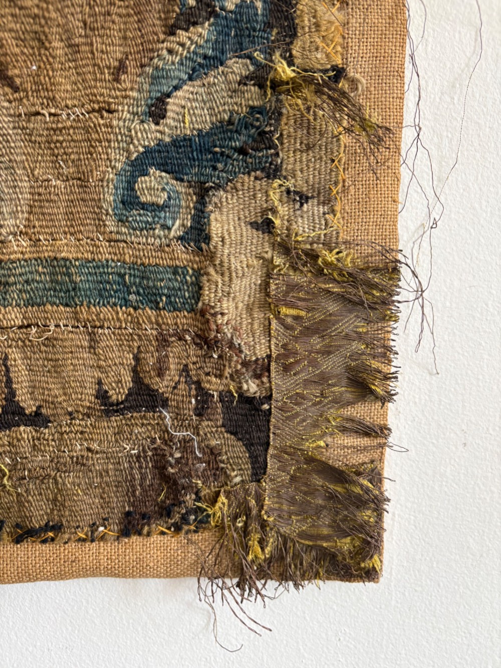 A vertical fragment of an antique hand-woven verdure tapestry featuring acanthus leaf motifs, mounted onto a natural linen backing. View V