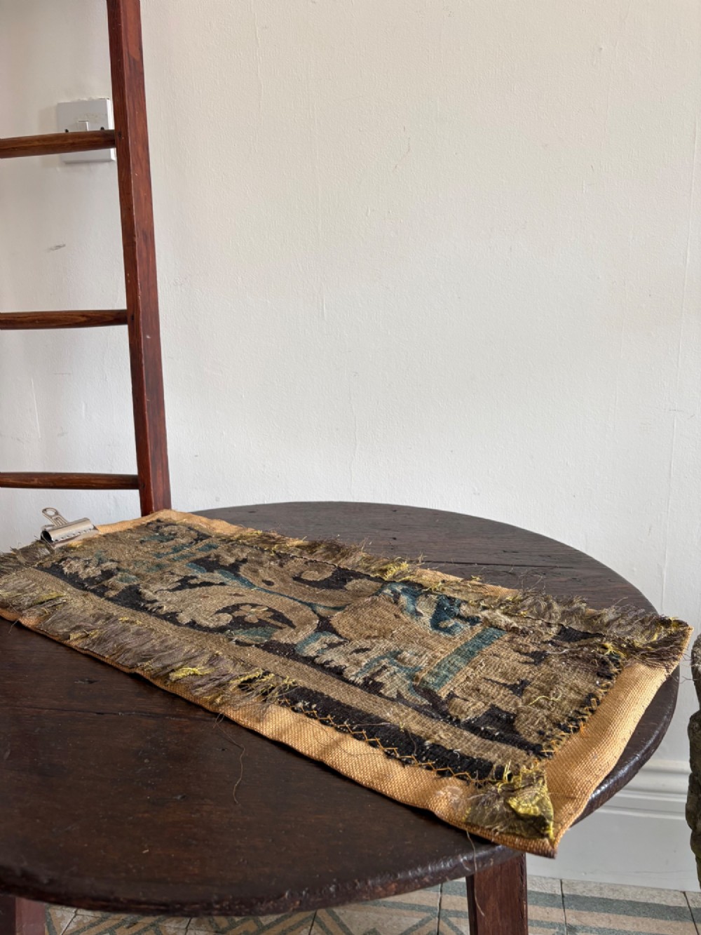 A vertical fragment of an antique hand-woven verdure tapestry featuring acanthus leaf motifs, mounted onto a natural linen backing. View X