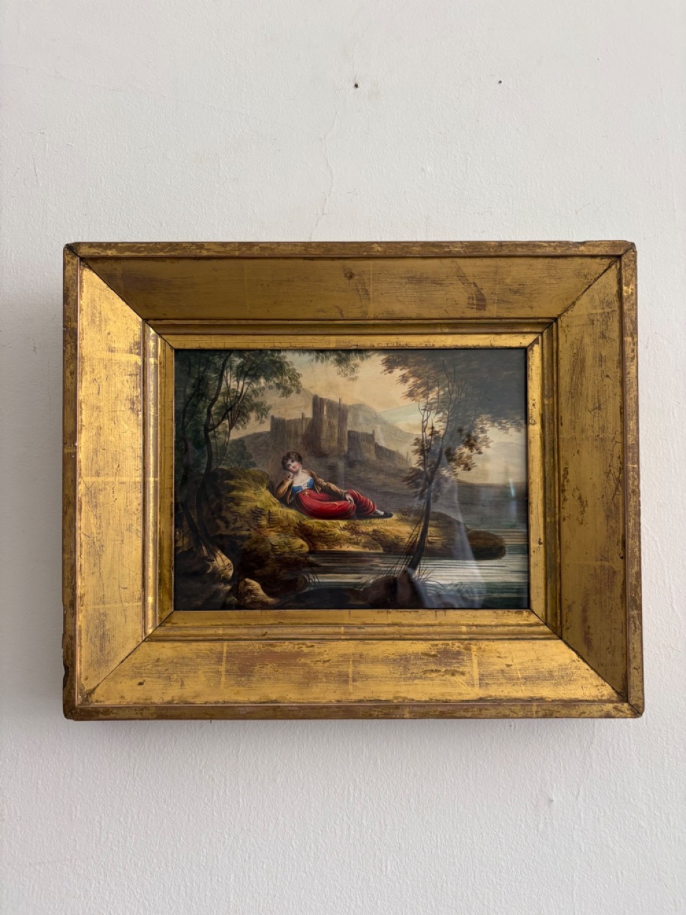 A 19th-century watercolour painting depicting a reclining figure in a landscape with ruins, set inside a broad giltwood frame.