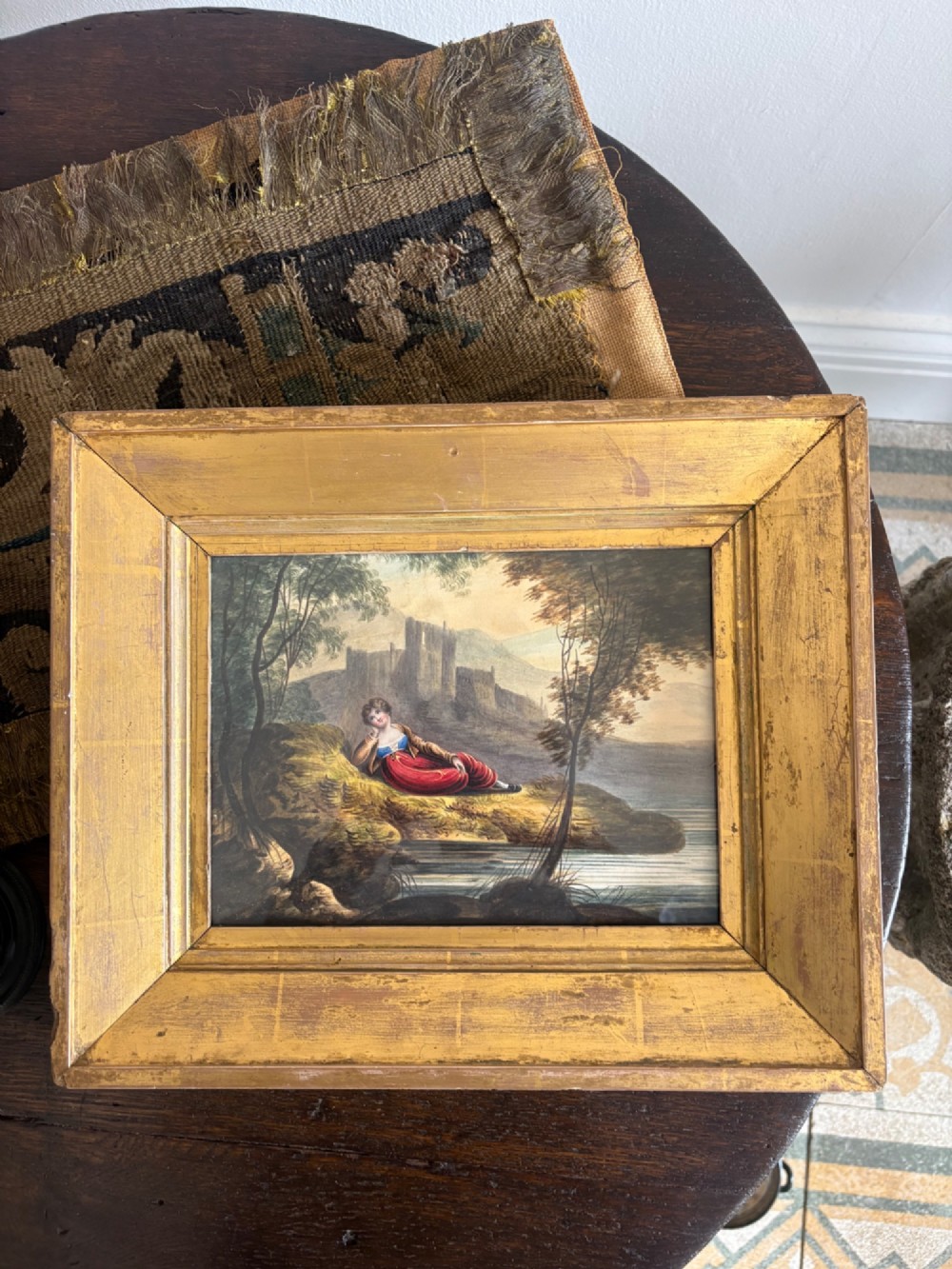 A 19th-century watercolour painting depicting a reclining figure in a landscape with ruins, set inside a broad giltwood frame. View IV