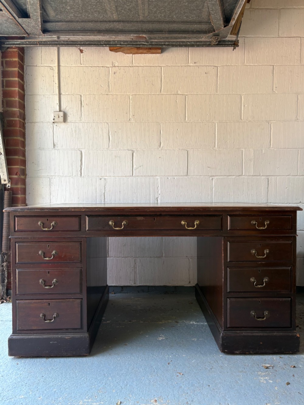 An antique dark mahogany pedestal desk featuring a green leather inset writing top, nine drawers with brass swan-neck handles, and twin pedestals on plinth bases.