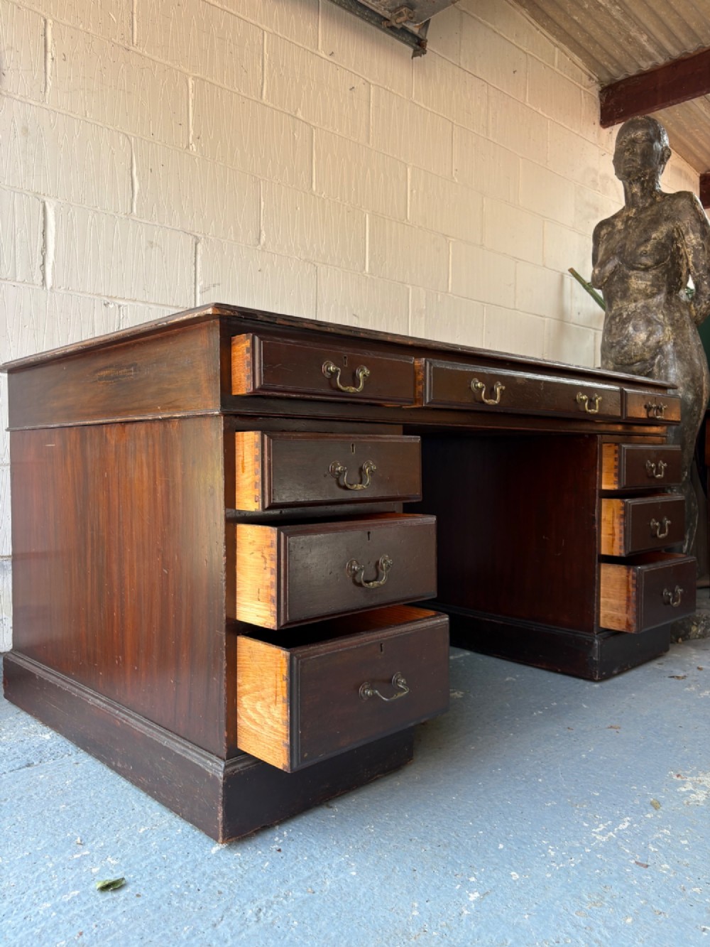 An antique dark mahogany pedestal desk featuring a green leather inset writing top, nine drawers with brass swan-neck handles, and twin pedestals on plinth bases. View VI
