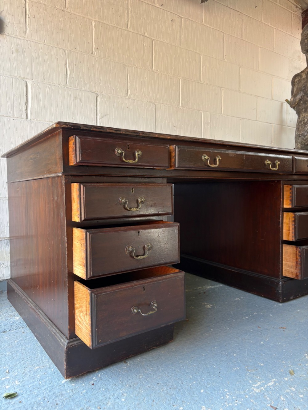 An antique dark mahogany pedestal desk featuring a green leather inset writing top, nine drawers with brass swan-neck handles, and twin pedestals on plinth bases. View VII