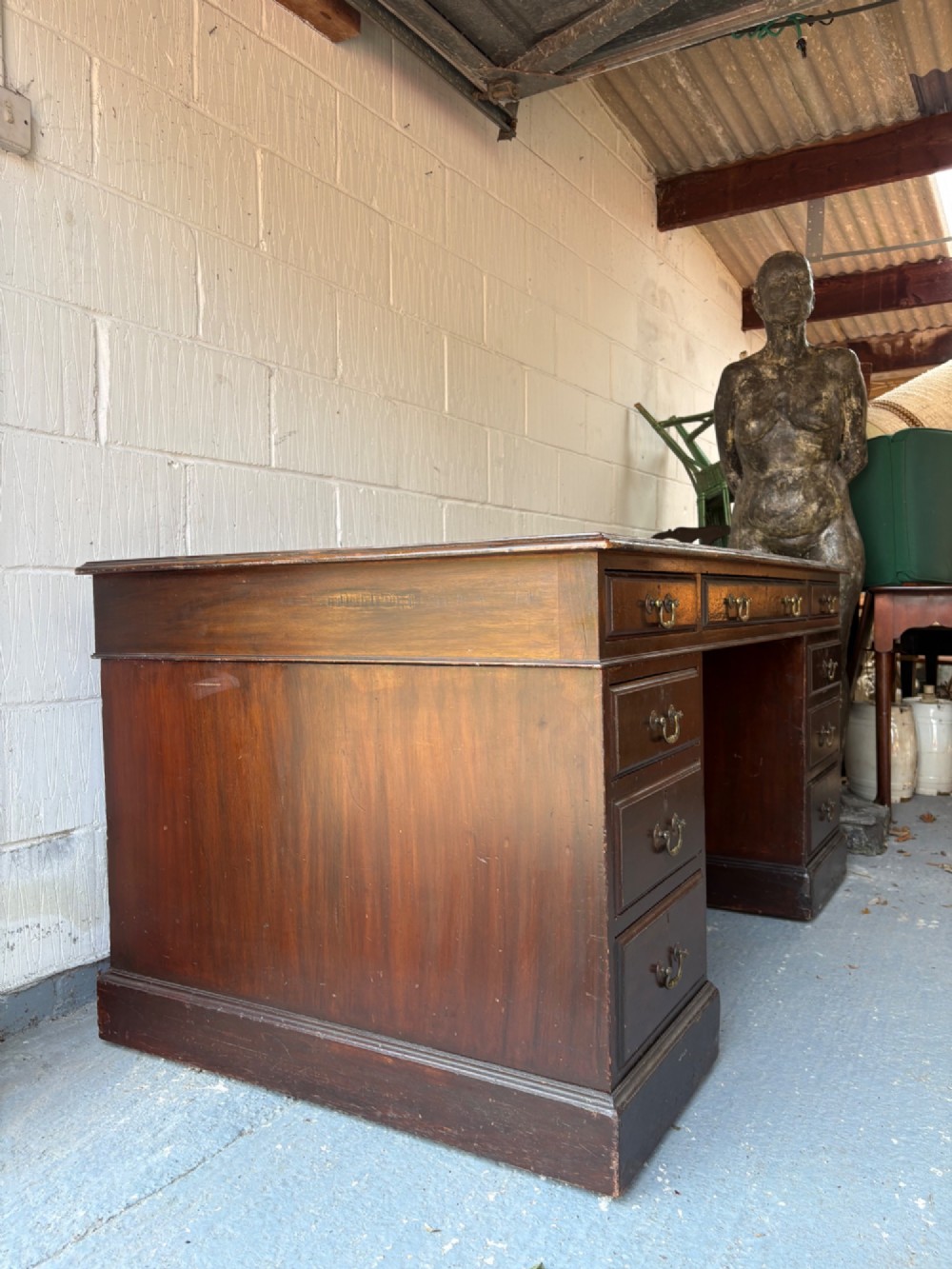 An antique dark mahogany pedestal desk featuring a green leather inset writing top, nine drawers with brass swan-neck handles, and twin pedestals on plinth bases. View X