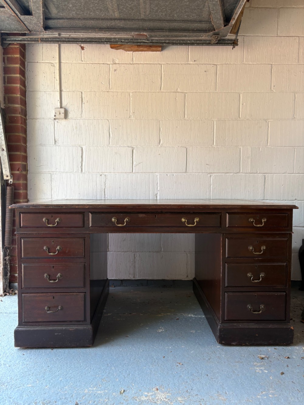 An antique dark mahogany pedestal desk featuring a green leather inset writing top, nine drawers with brass swan-neck handles, and twin pedestals on plinth bases. View XIV