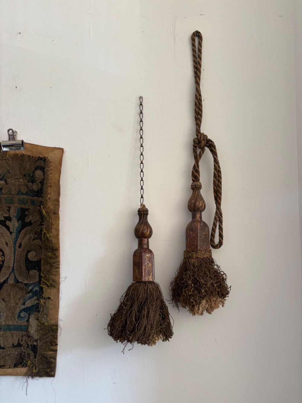 A pair of 19th-century Venetian curtain tiebacks with carved giltwood turned tops and dense fibrous tassels suspended by a chain and cord.