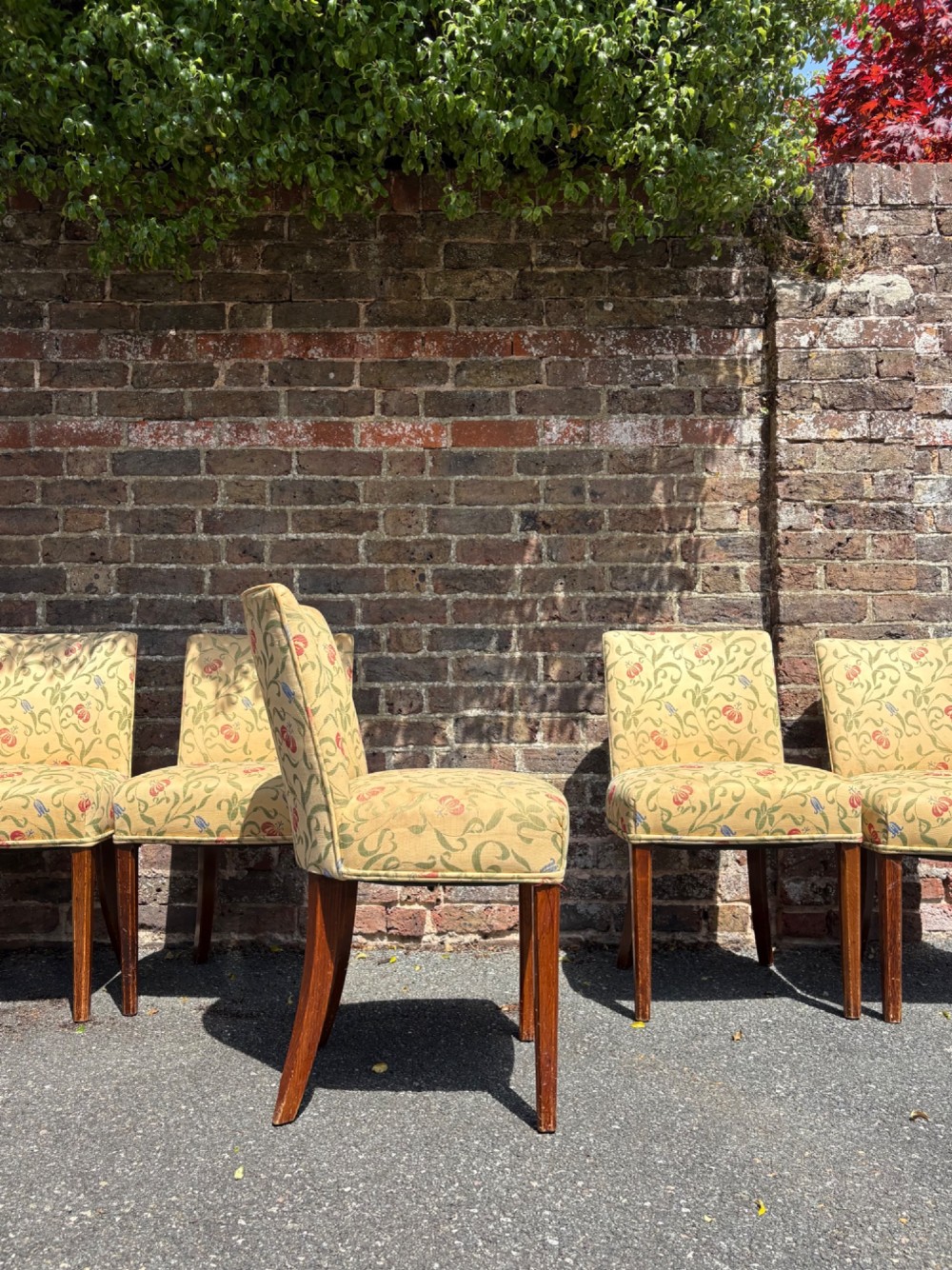 A row of 1930s Art Deco dining chairs featuring yellow floral pattern upholstery and dark oak tapered legs. View II