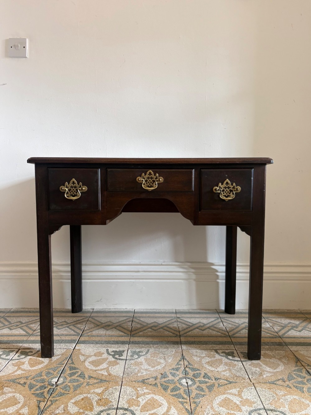 A George III style mahogany lowboy table featuring three drawers with decorative brass handles and an arched apron.