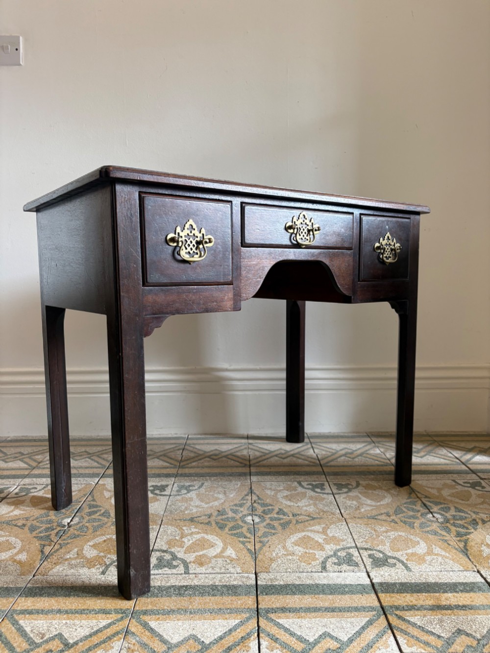 A George III style mahogany lowboy table featuring three drawers with decorative brass handles and an arched apron. View II