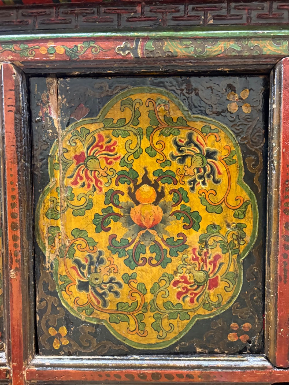A 19th-century Tibetan wooden cabinet featuring four central hand-painted floral panels framed in red and gold mineral pigments. View V