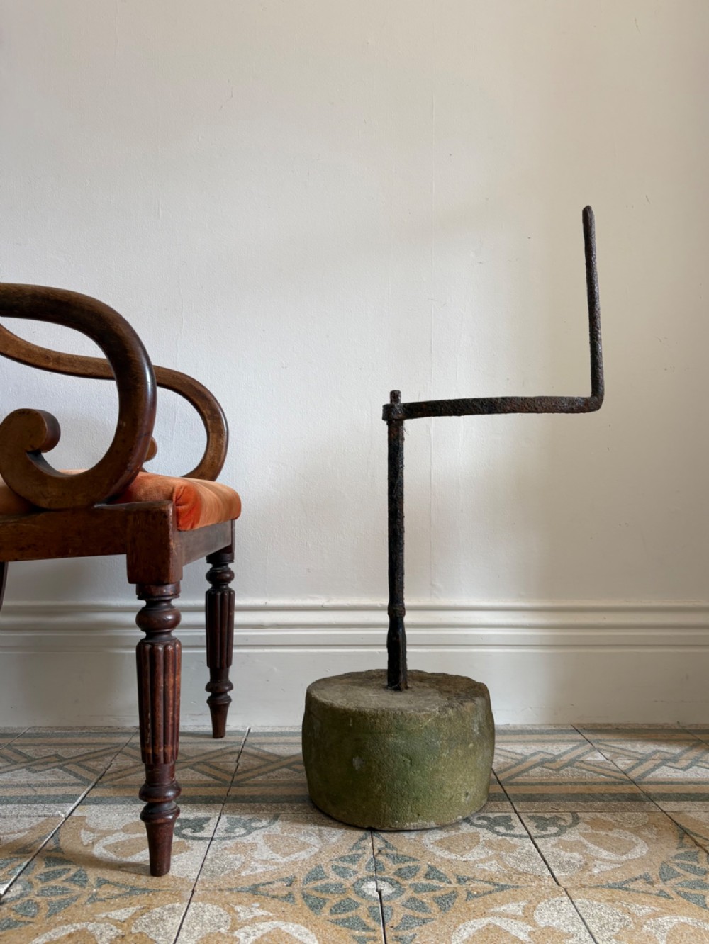 An 18th-century cylindrical carved stone weight featuring an upright hand-forged iron handle attachment.