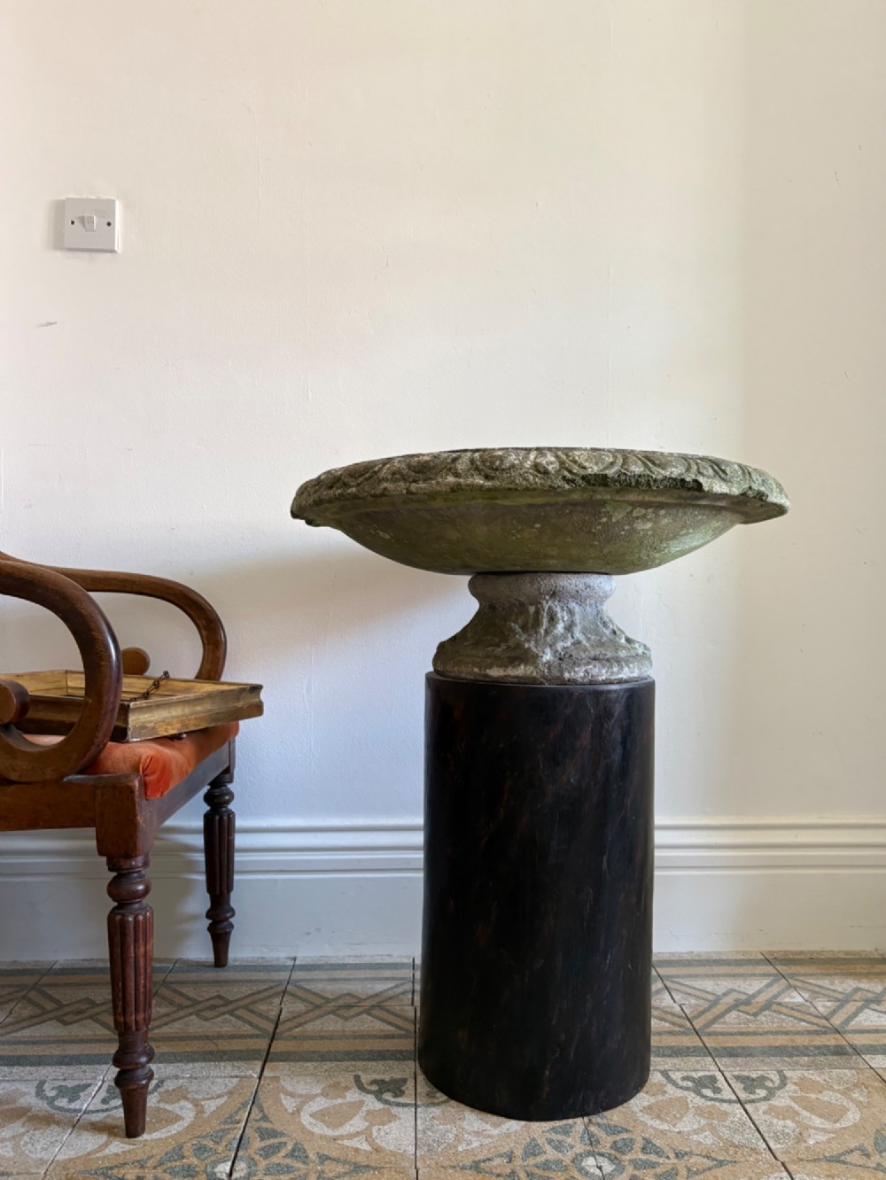 A shallow Neoclassical cast stone birdbath planter with a low moulded pedestal base, displaying a weathered grey and green patinated surface.