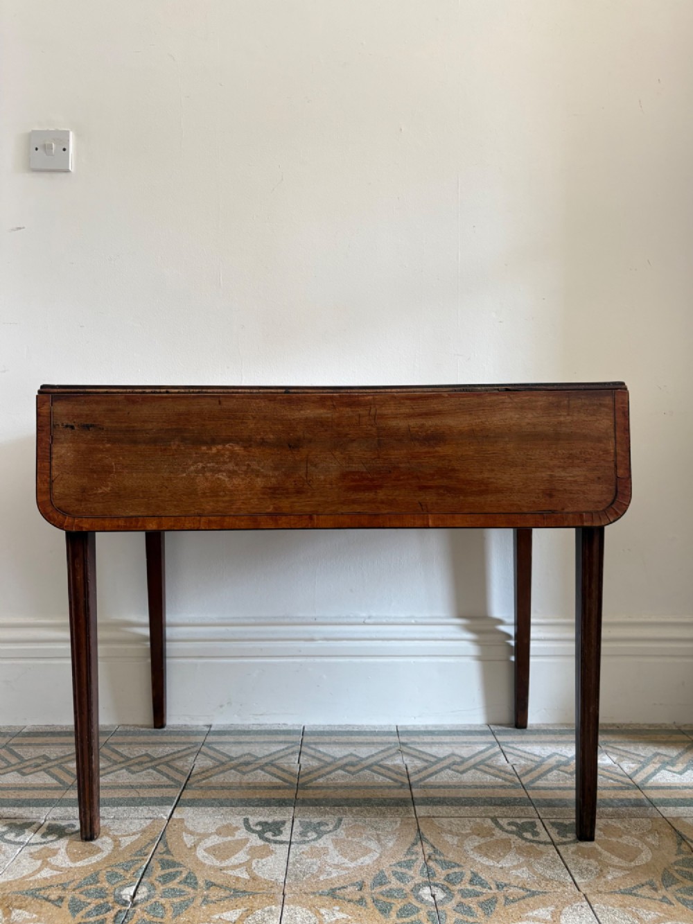 A Georgian mahogany drop-leaf Pembroke table featuring a shaped apron and tapered square legs.