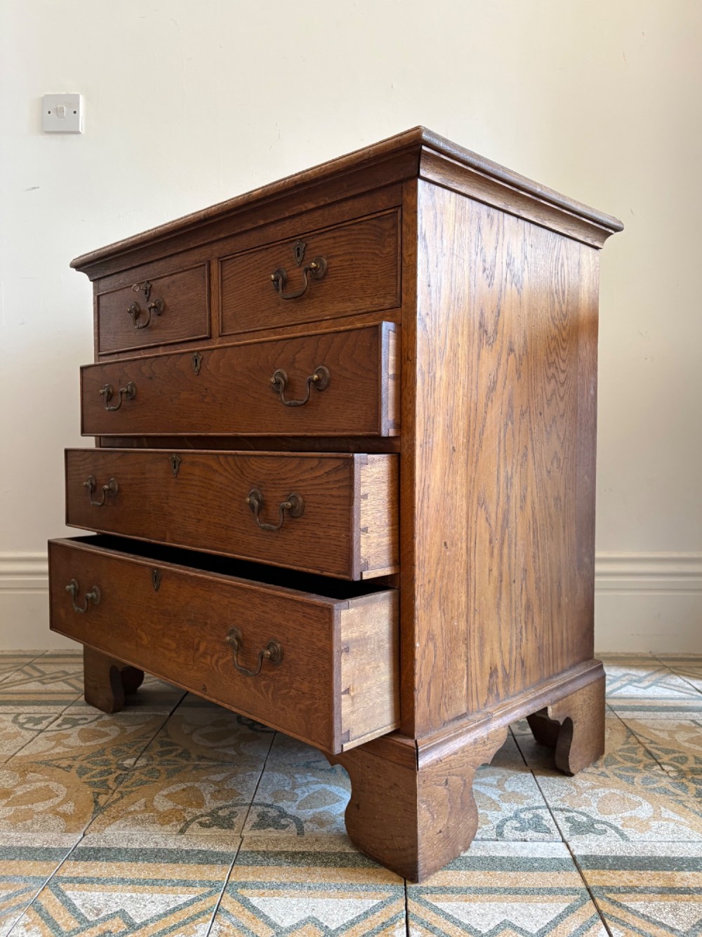 A George III style medium oak chest of drawers featuring two short drawers above three long drawers, resting on shaped bracket feet with brass handles. View II