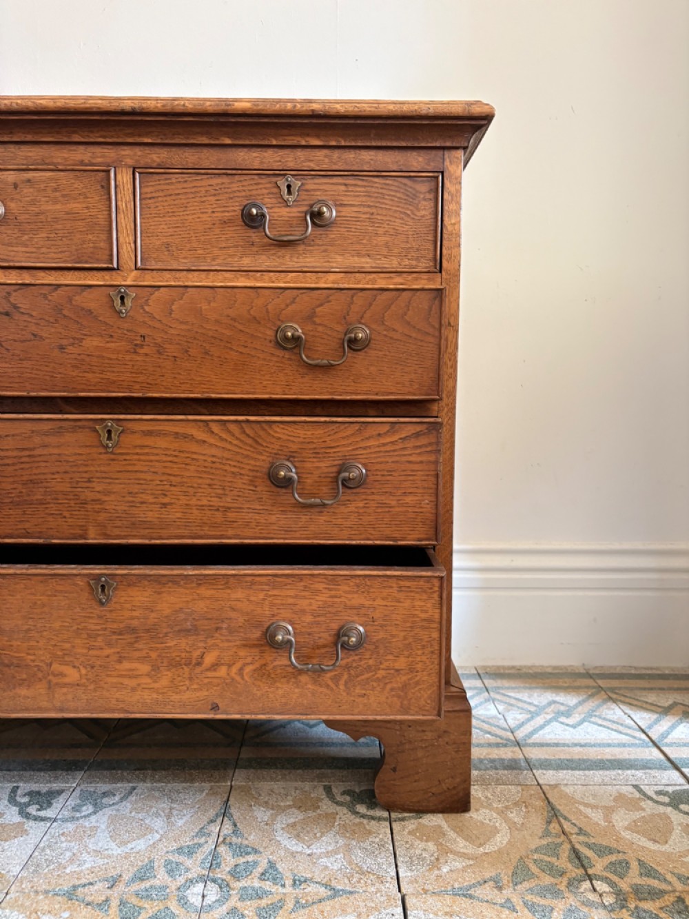 A George III style medium oak chest of drawers featuring two short drawers above three long drawers, resting on shaped bracket feet with brass handles. View V