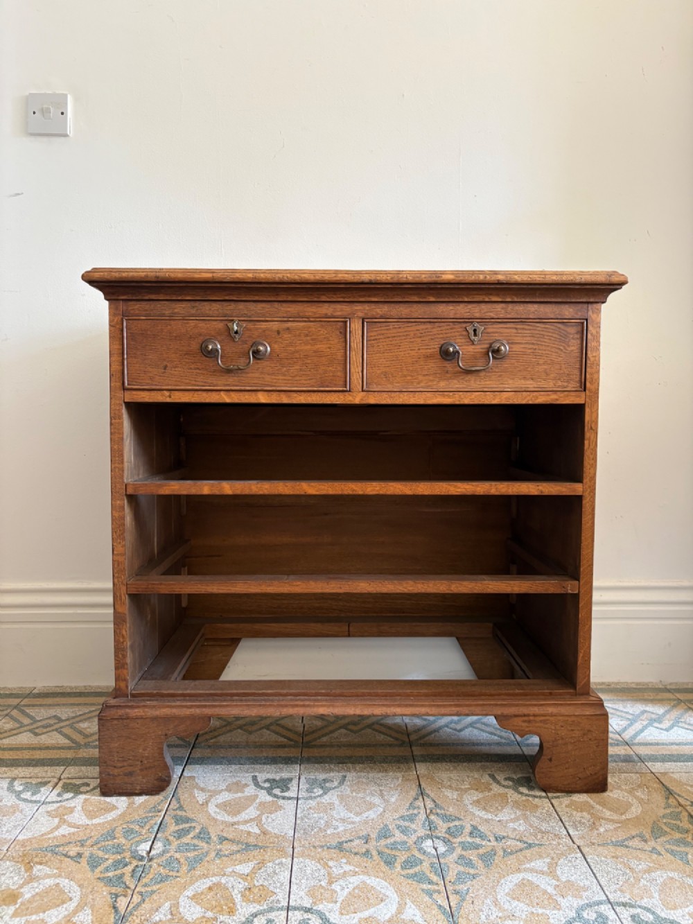 A George III style medium oak chest of drawers featuring two short drawers above three long drawers, resting on shaped bracket feet with brass handles. View IX