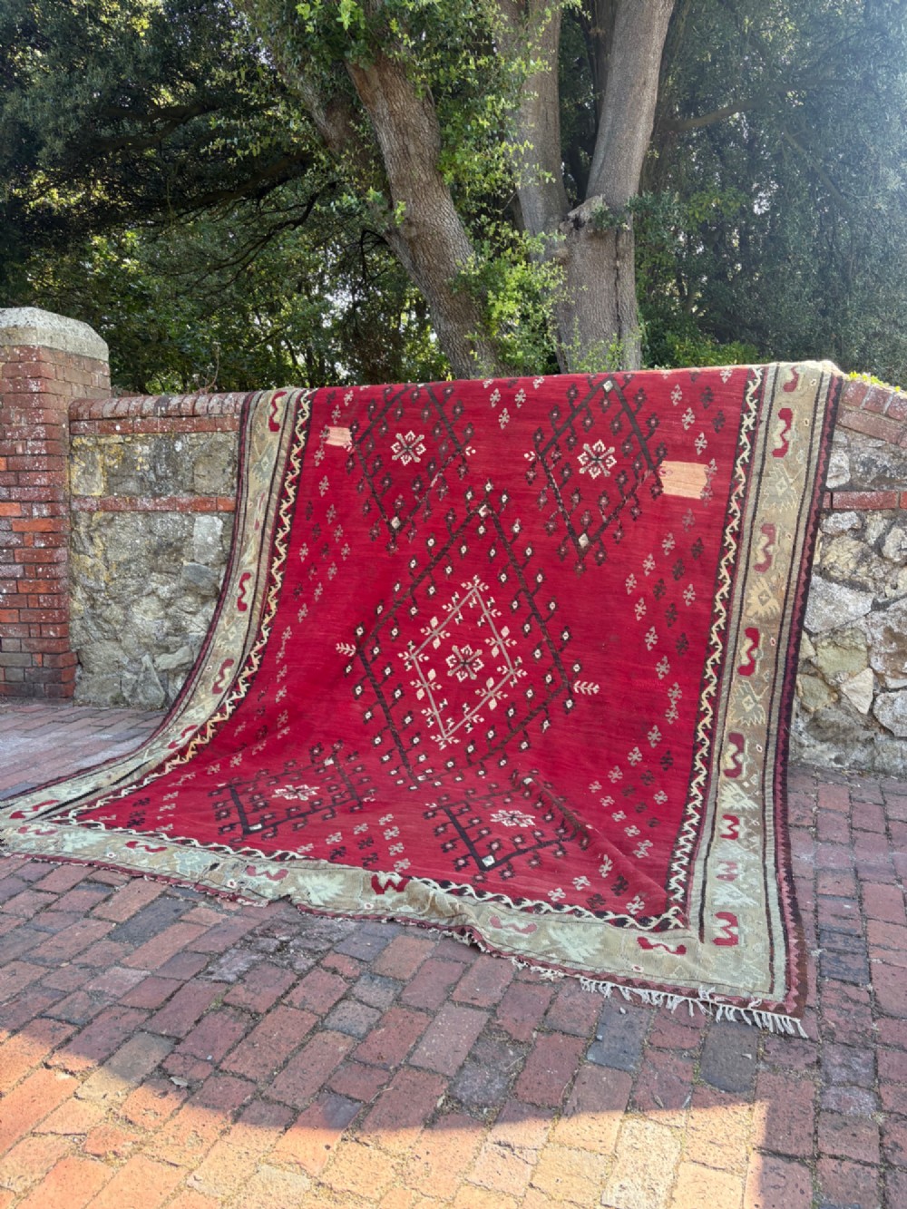 A large handwoven Anatolian flatweave kilim rug featuring a vivid red field patterned with dark geometric diamond motifs and framed by a light beige border.