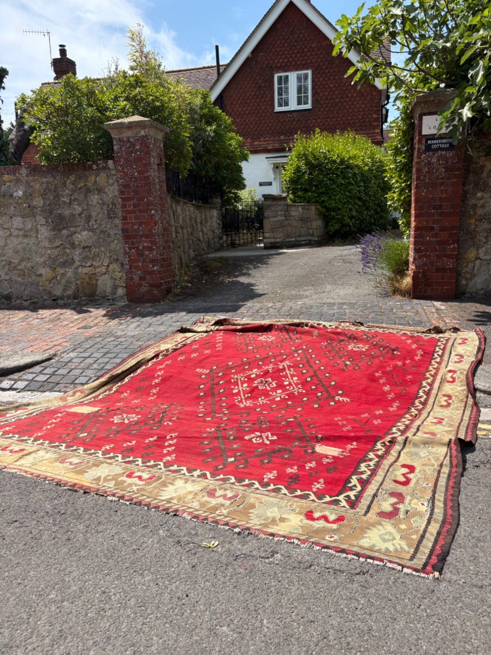 A large handwoven Anatolian flatweave kilim rug featuring a vivid red field patterned with dark geometric diamond motifs and framed by a light beige border. View III