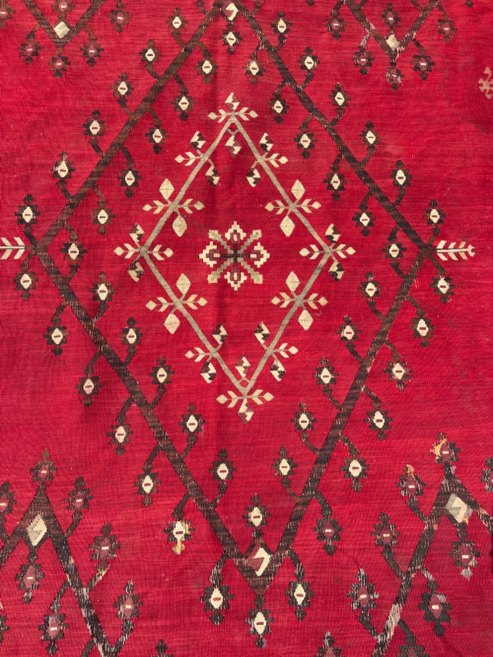 A large handwoven Anatolian flatweave kilim rug featuring a vivid red field patterned with dark geometric diamond motifs and framed by a light beige border. View IV