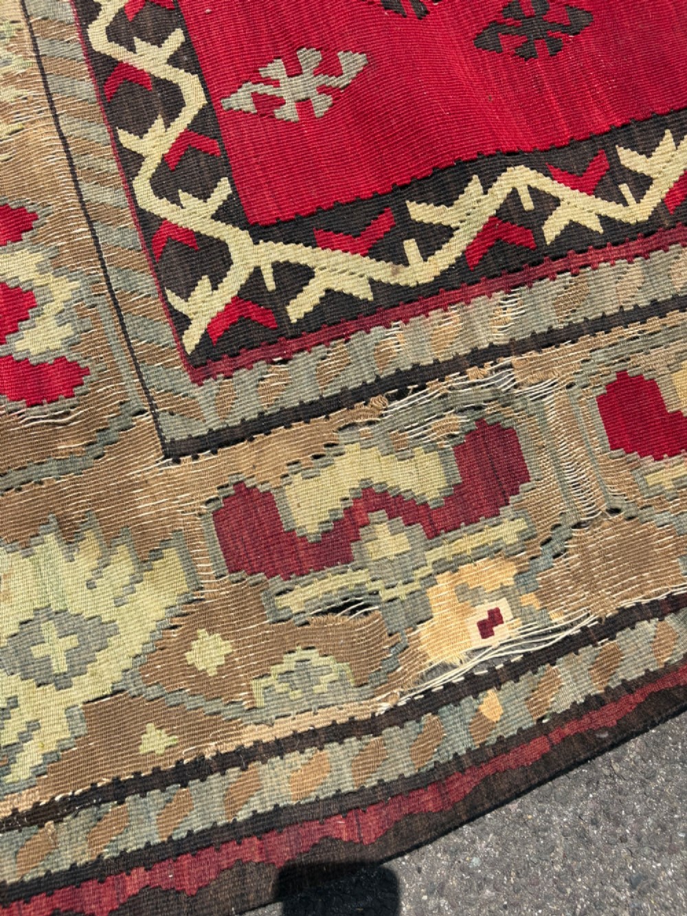 A large handwoven Anatolian flatweave kilim rug featuring a vivid red field patterned with dark geometric diamond motifs and framed by a light beige border. View V