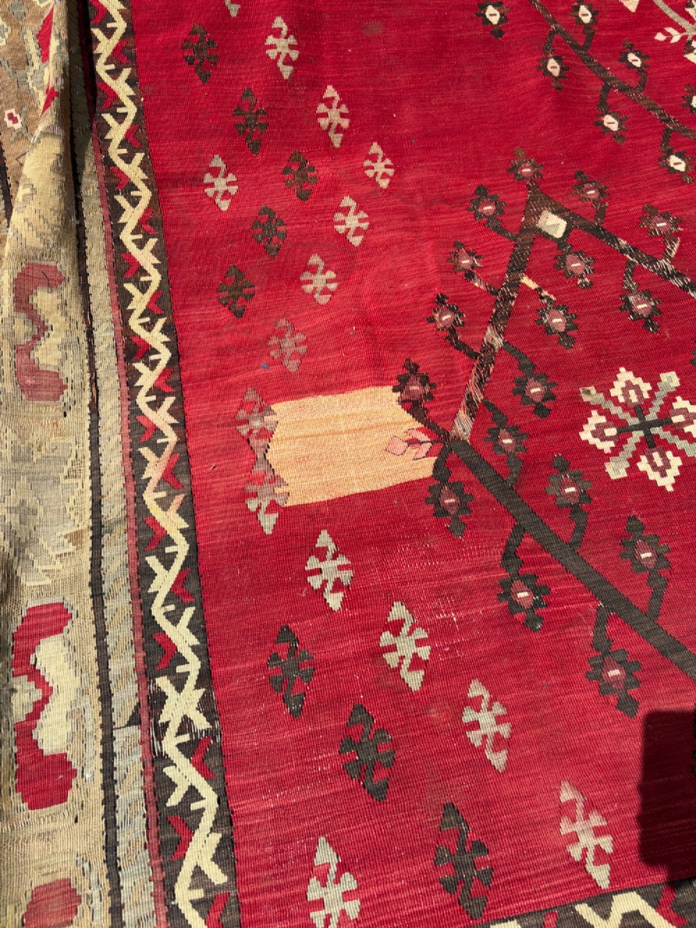 A large handwoven Anatolian flatweave kilim rug featuring a vivid red field patterned with dark geometric diamond motifs and framed by a light beige border. View VII