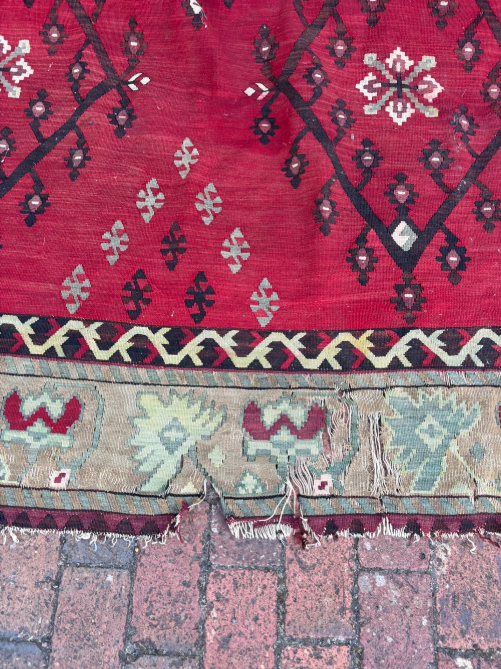 A large handwoven Anatolian flatweave kilim rug featuring a vivid red field patterned with dark geometric diamond motifs and framed by a light beige border. View X