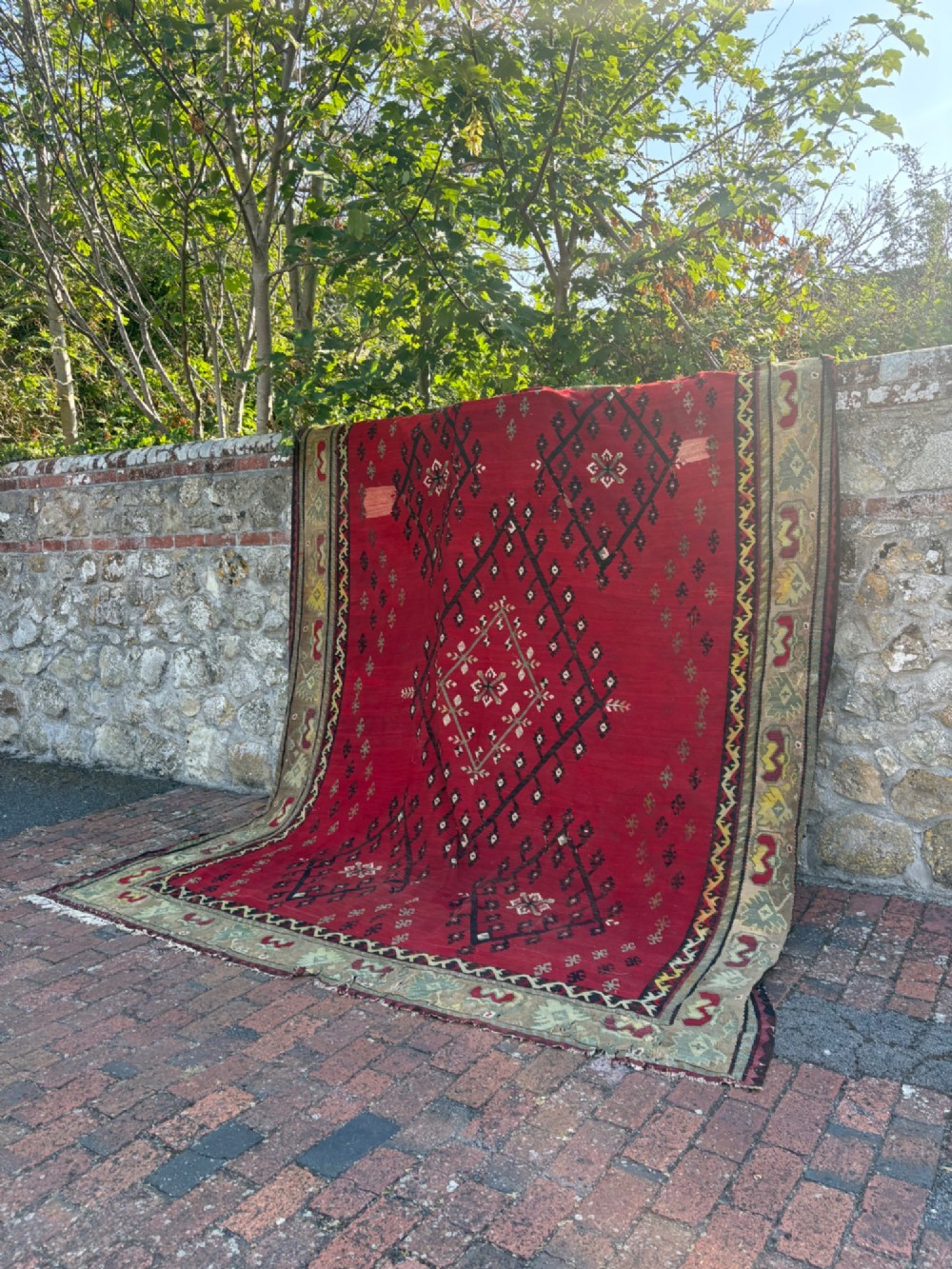 A large handwoven Anatolian flatweave kilim rug featuring a vivid red field patterned with dark geometric diamond motifs and framed by a light beige border. View XIII