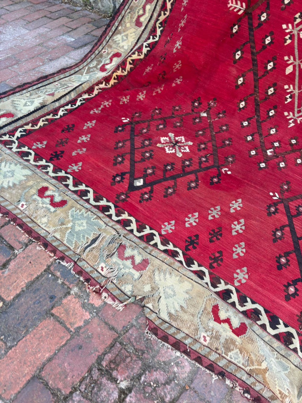 A large handwoven Anatolian flatweave kilim rug featuring a vivid red field patterned with dark geometric diamond motifs and framed by a light beige border. View XV