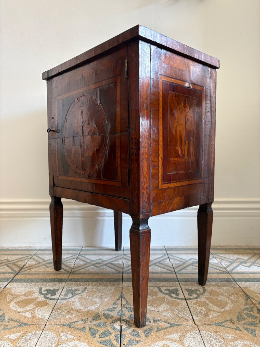 An 18th-century Italian Neoclassical walnut bedside cabinet featuring a central circular figurative marquetry panel on the front door, supported by square tapered legs. View II