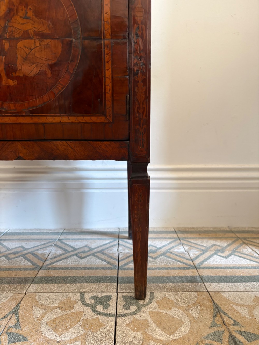 An 18th-century Italian Neoclassical walnut bedside cabinet featuring a central circular figurative marquetry panel on the front door, supported by square tapered legs. View V