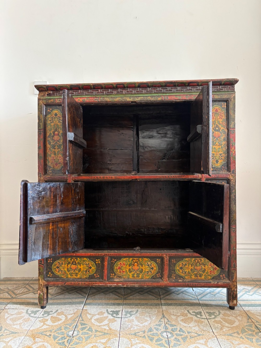 A 19th-century Tibetan wooden cabinet featuring four central hand-painted floral panels framed in red and gold mineral pigments. View X