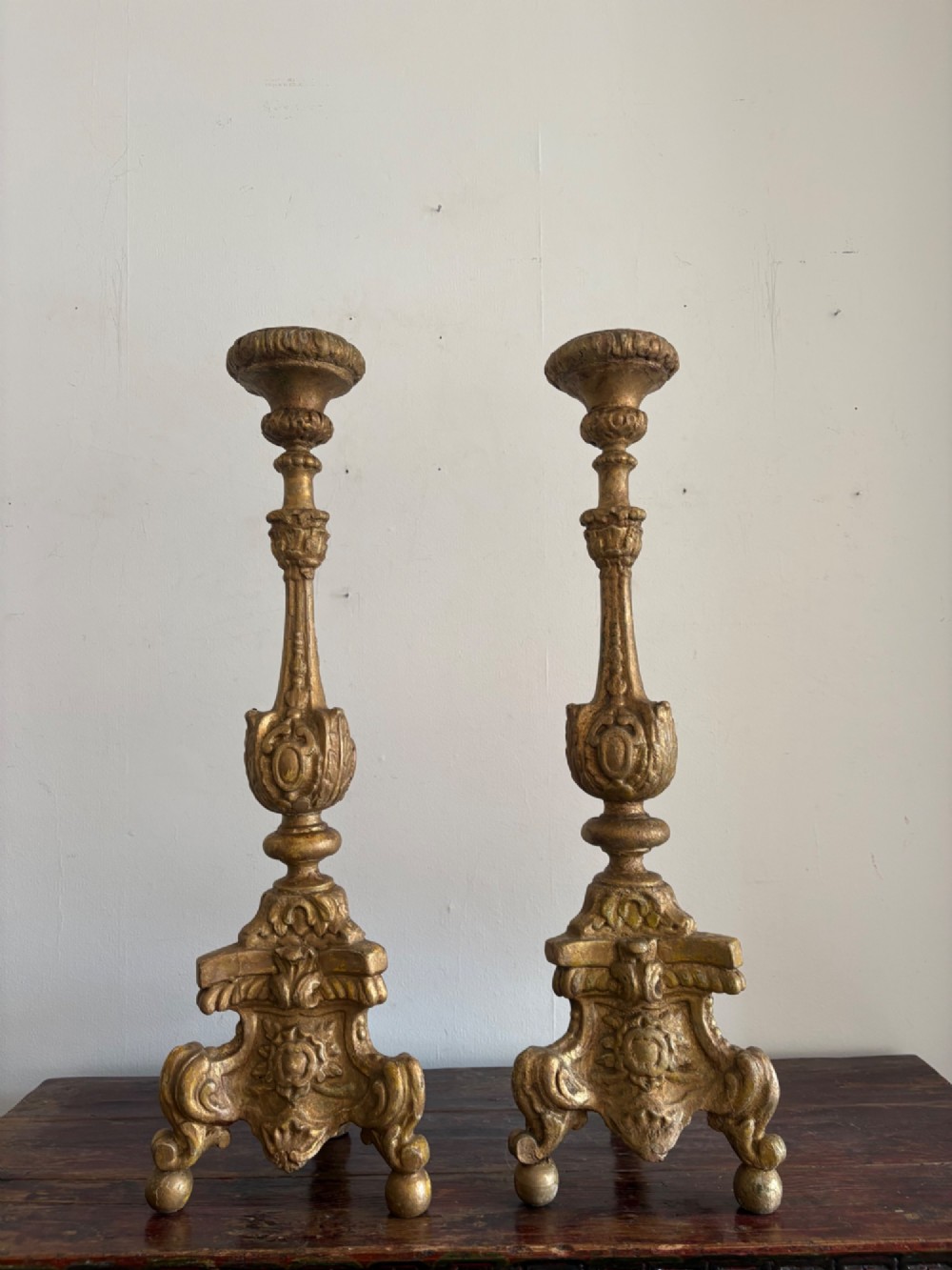A pair of 18th-century Italian Baroque carved giltwood altar candlesticks featuring triform bases with scrollwork and tall baluster stems. View IV