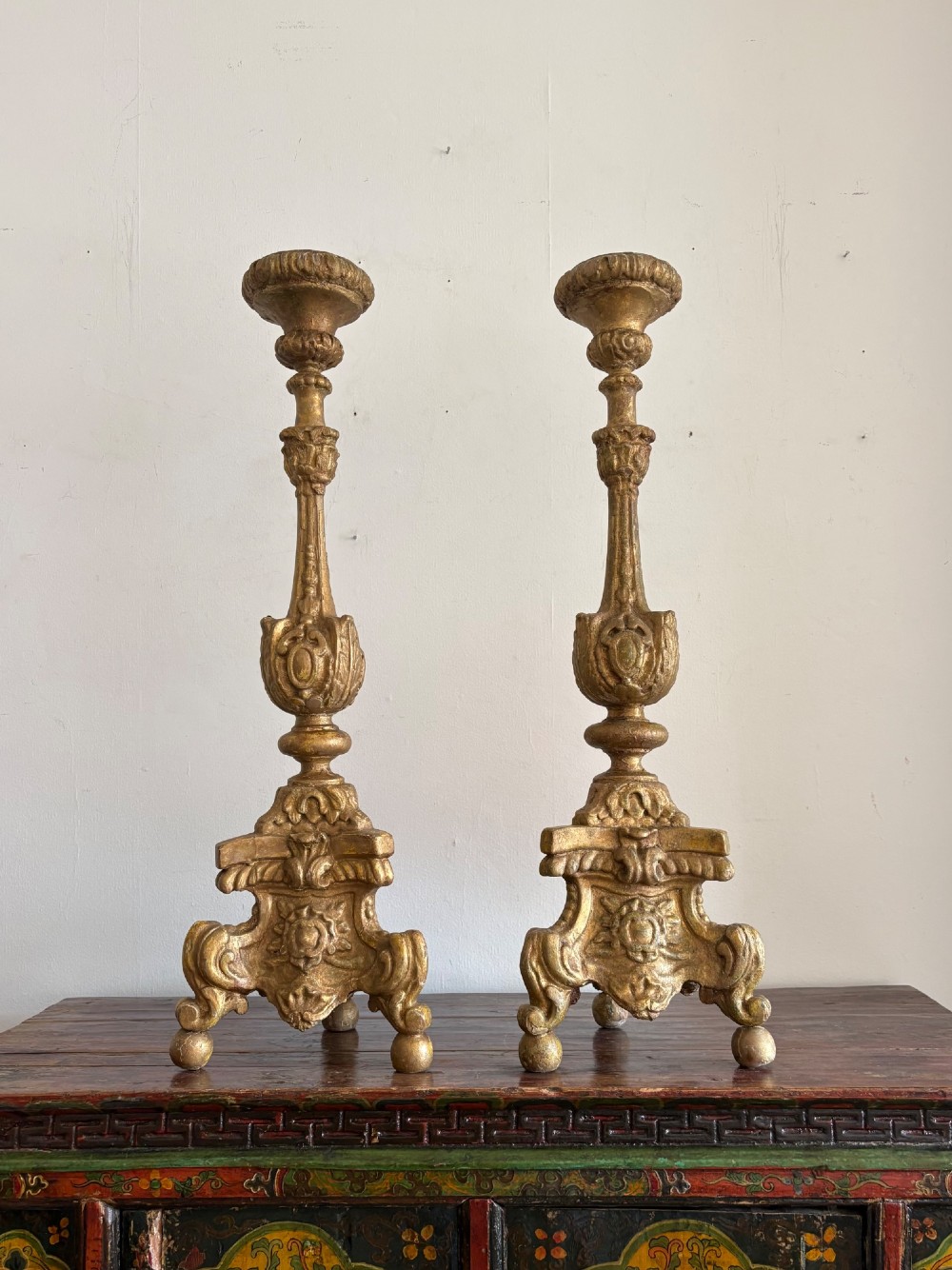 A pair of 18th-century Italian Baroque carved giltwood altar candlesticks featuring triform bases with scrollwork and tall baluster stems.