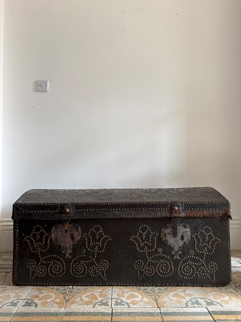 An 18th-century Dutch dark brown leather trunk featuring a domed lid, intricate brass studding in scrolling floral patterns, and iron lock hardware.
