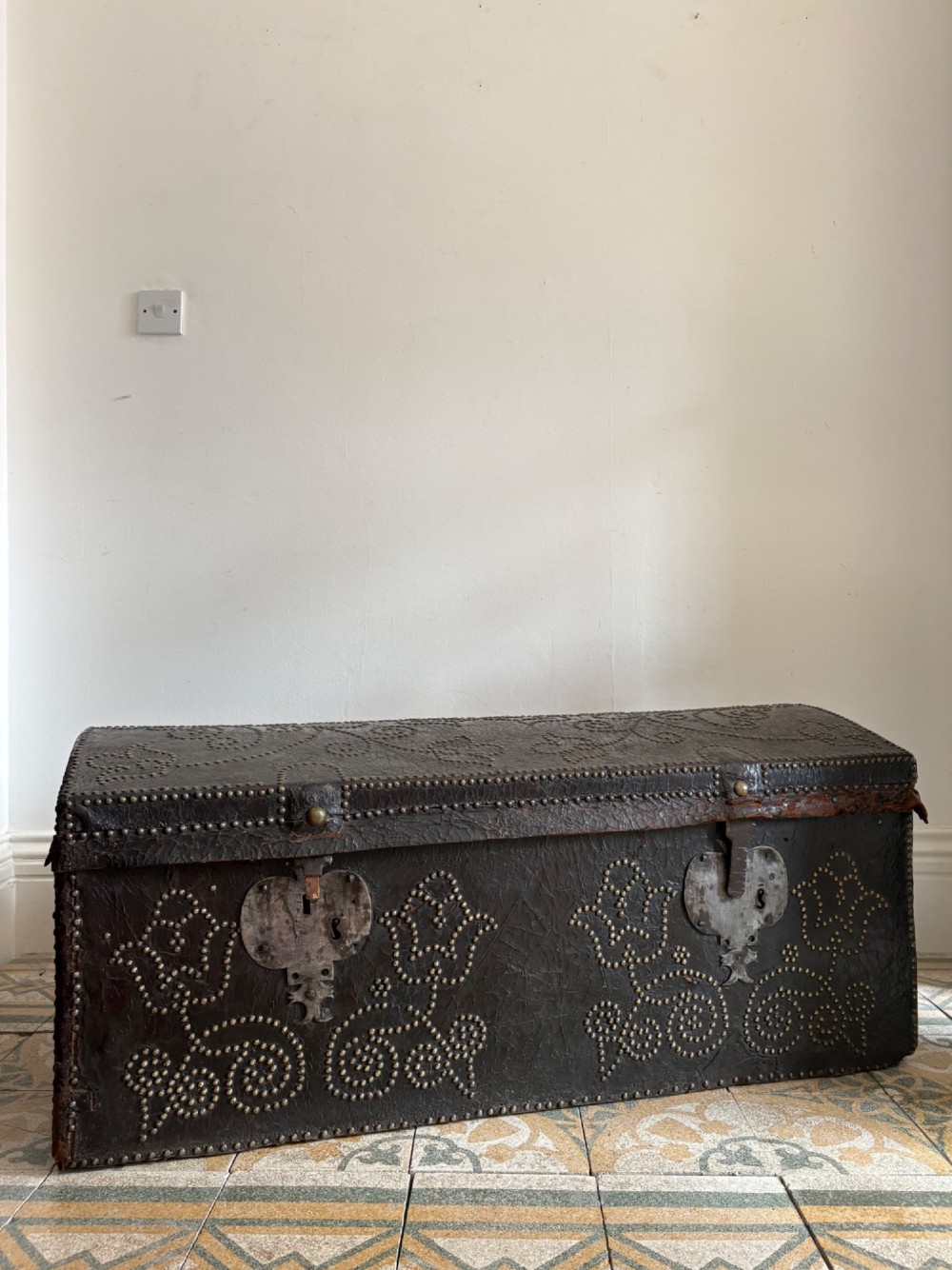 An 18th-century Dutch dark brown leather trunk featuring a domed lid, intricate brass studding in scrolling floral patterns, and iron lock hardware. View IV