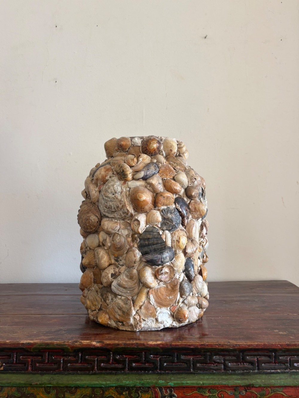A cylindrical antique vase completely encrusted with an assortment of natural sea shells set into a mortar matrix.