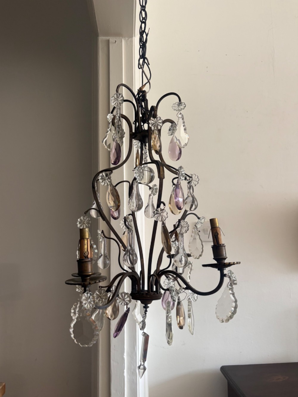 A four-branch French Rococo style gilt bronze chandelier decorated with clear, grey, and violet crystal drops.