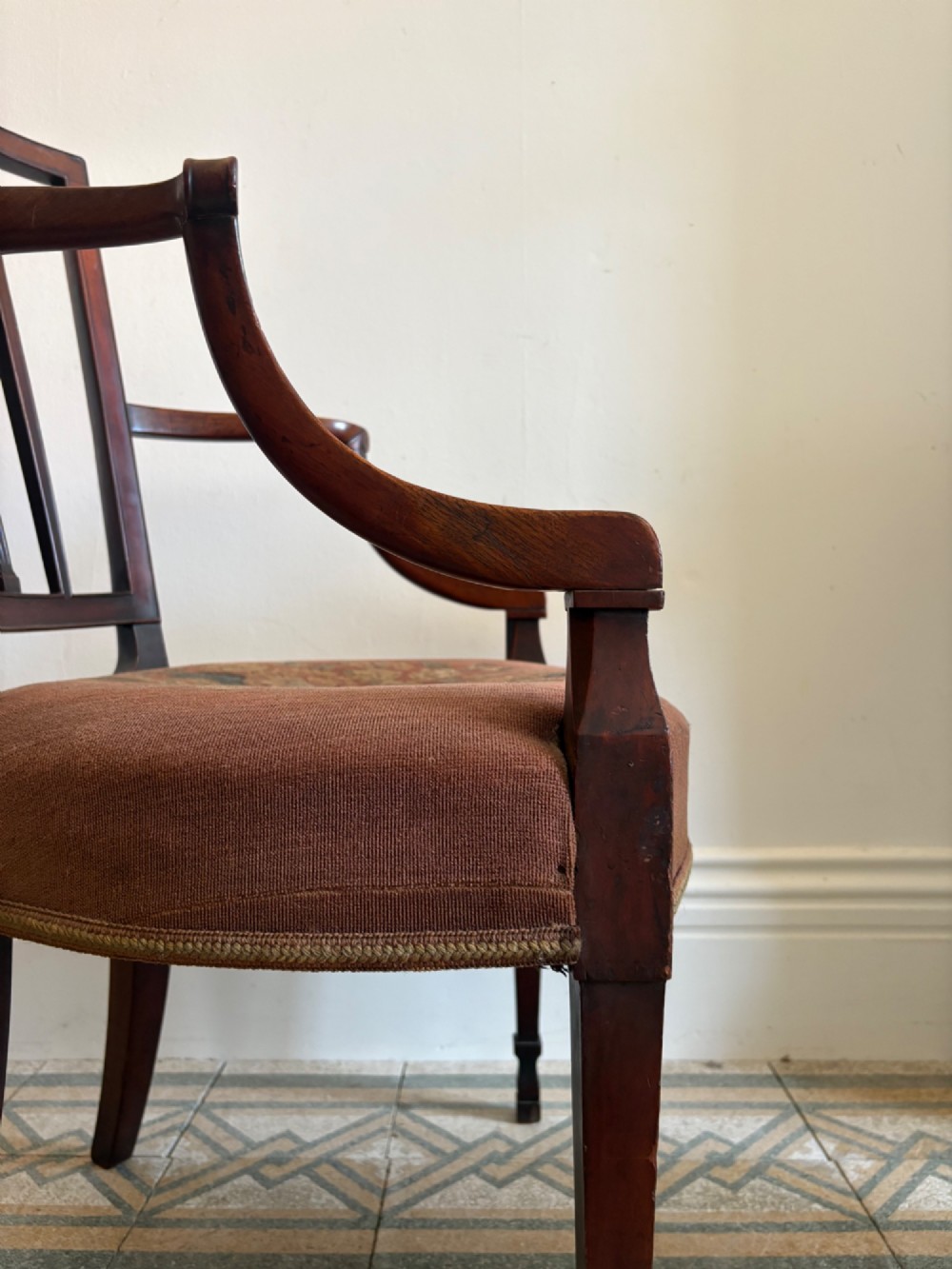 A late 18th-century Georgian mahogany open armchair featuring a carved back splat with a central rosewood roundel, swept armrests, and reddish-brown fabric upholstery. View V