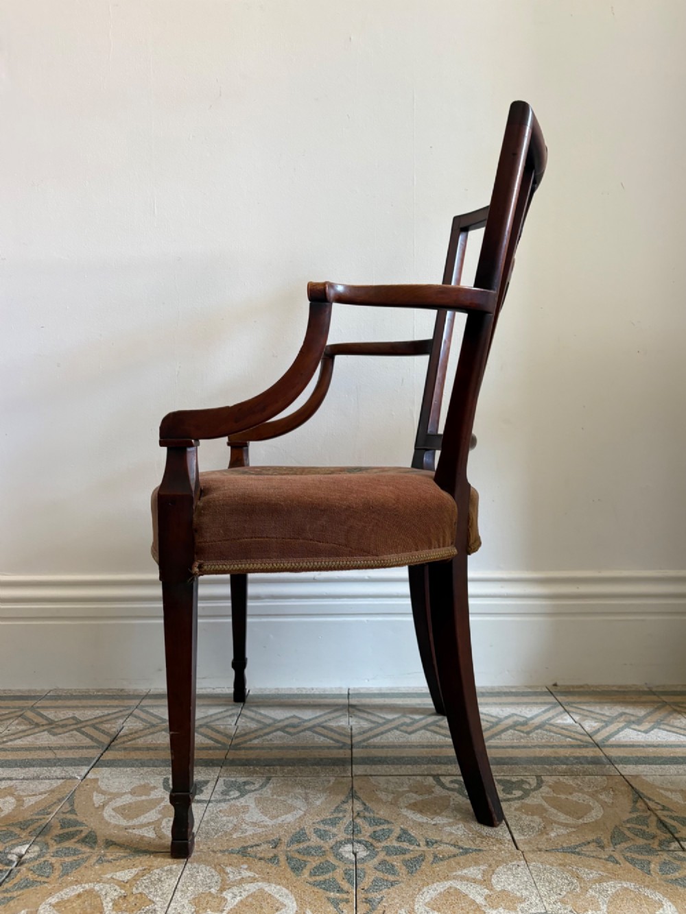 A late 18th-century Georgian mahogany open armchair featuring a carved back splat with a central rosewood roundel, swept armrests, and reddish-brown fabric upholstery. View VI