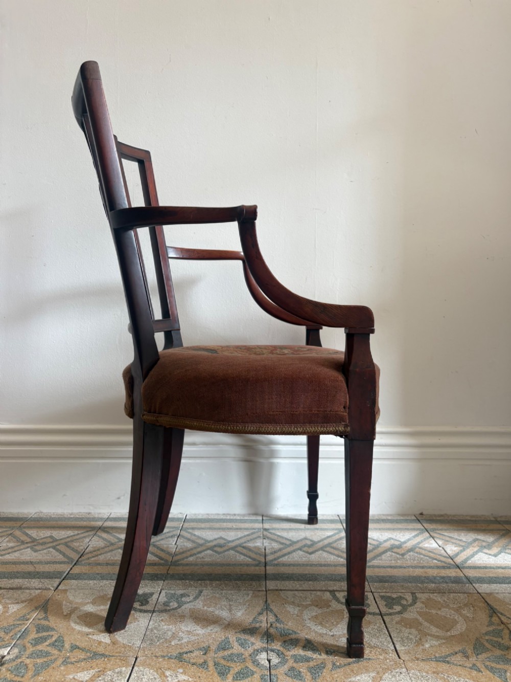A late 18th-century Georgian mahogany open armchair featuring a carved back splat with a central rosewood roundel, swept armrests, and reddish-brown fabric upholstery. View XV