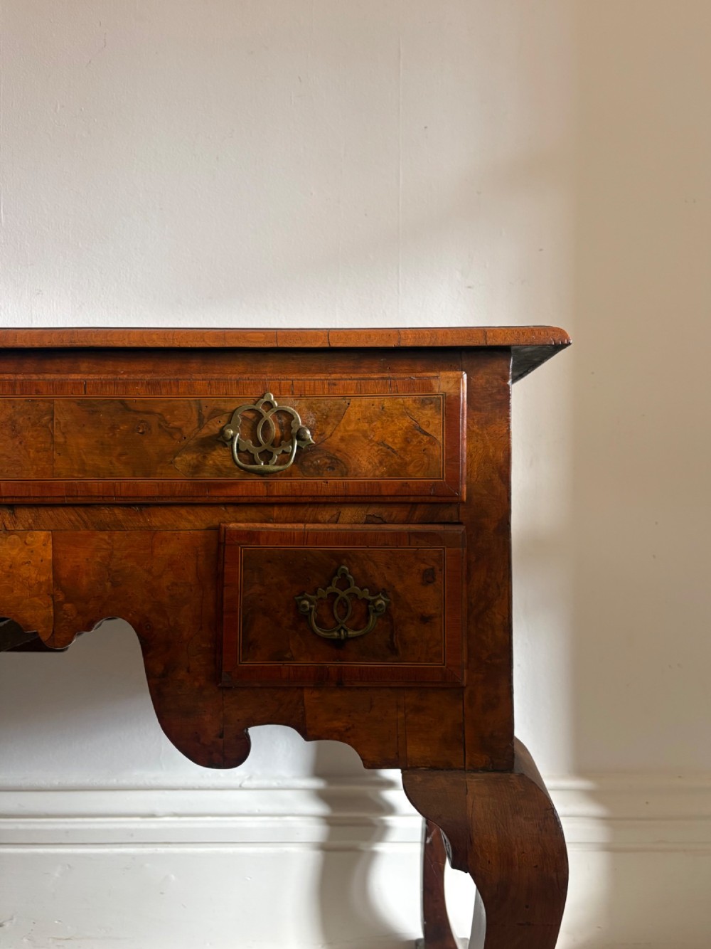An early 18th-century figured walnut lowboy side table featuring three drawers, a shaped apron, brass handles, and cabriole legs. View II
