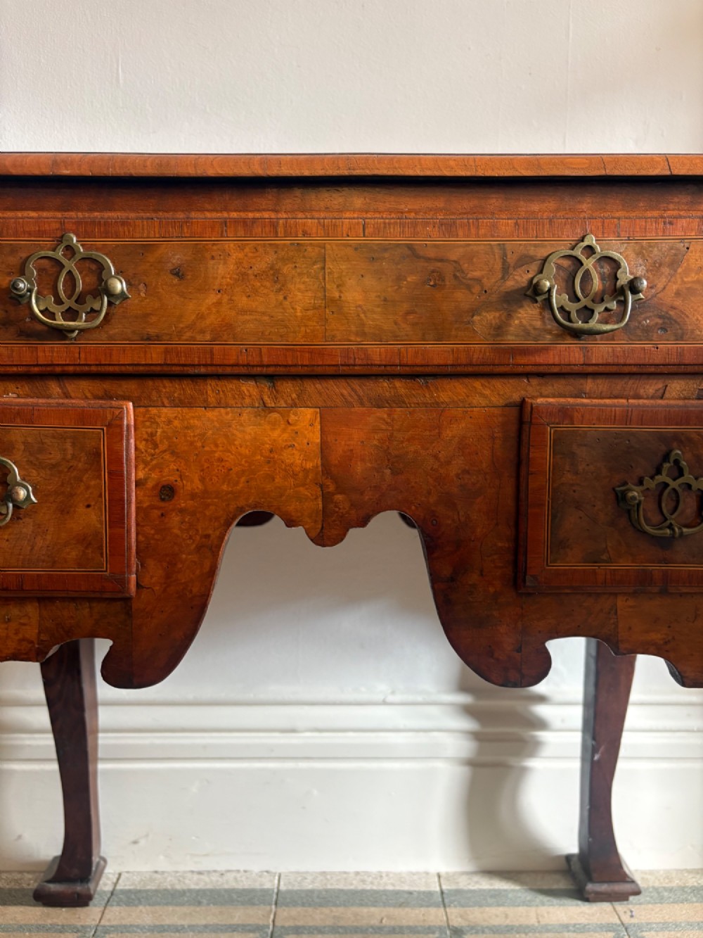 An early 18th-century figured walnut lowboy side table featuring three drawers, a shaped apron, brass handles, and cabriole legs. View III