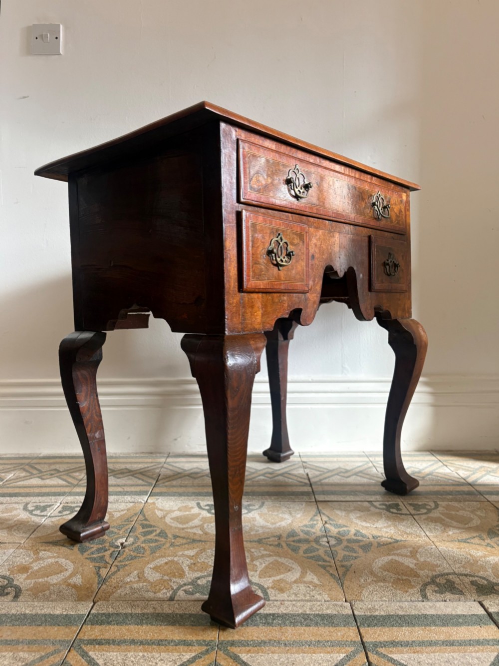 An early 18th-century figured walnut lowboy side table featuring three drawers, a shaped apron, brass handles, and cabriole legs. View IV