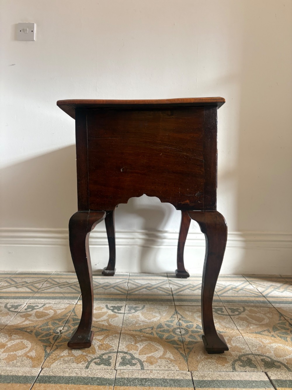 An early 18th-century figured walnut lowboy side table featuring three drawers, a shaped apron, brass handles, and cabriole legs. View V