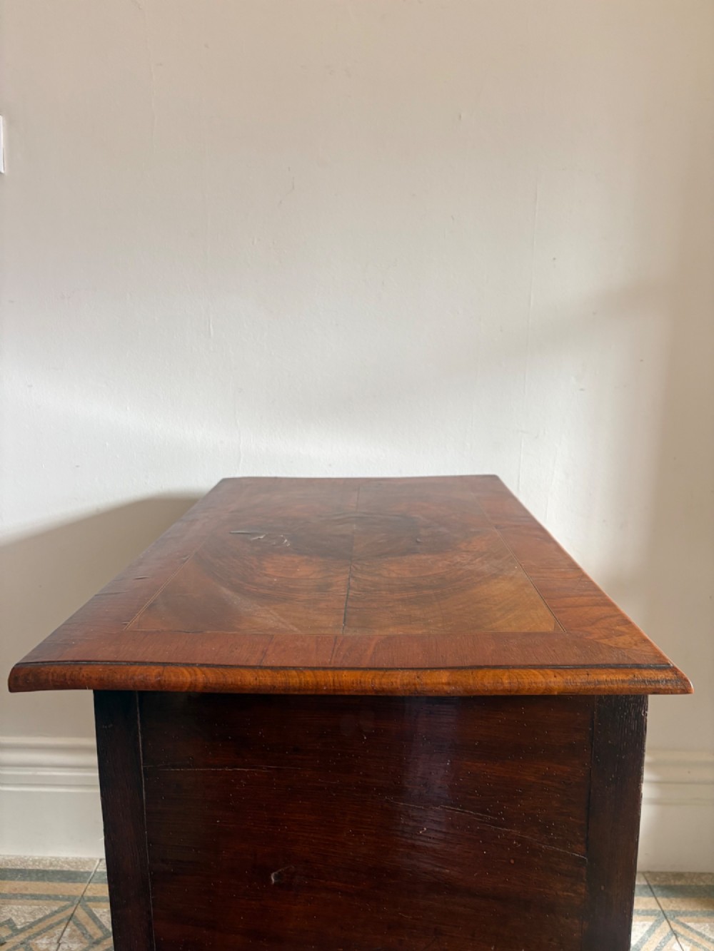 An early 18th-century figured walnut lowboy side table featuring three drawers, a shaped apron, brass handles, and cabriole legs. View X