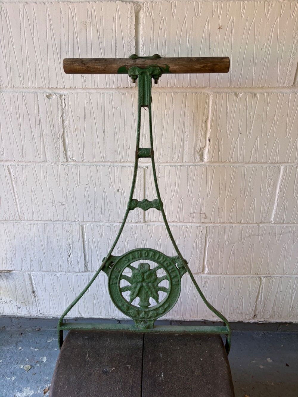 An antique cast iron garden roller featuring a green painted openwork frame with circular crest, a split drum cylinder, and a wooden handle bar. View II