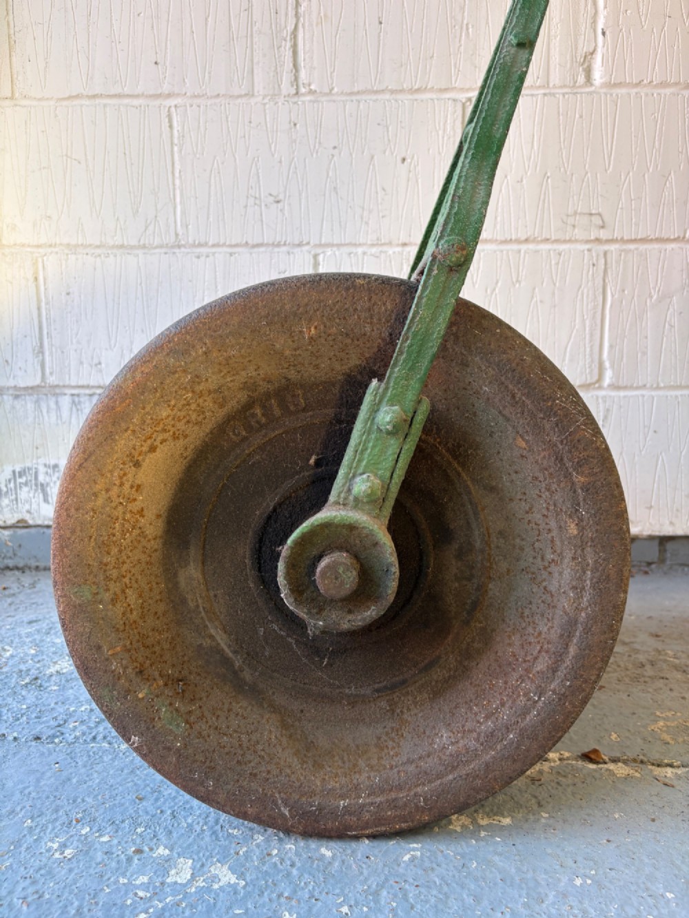 An antique cast iron garden roller featuring a green painted openwork frame with circular crest, a split drum cylinder, and a wooden handle bar. View V