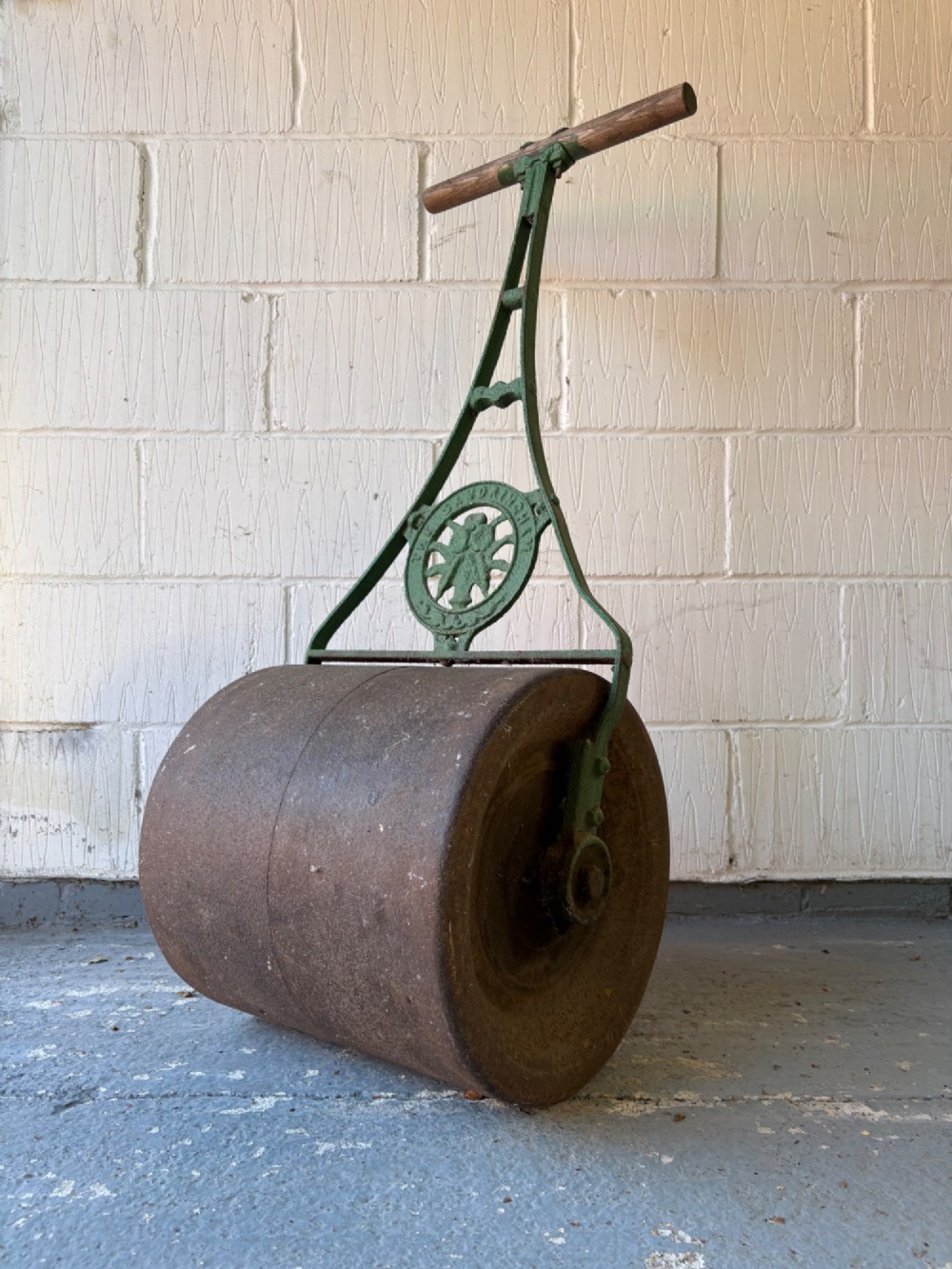 An antique cast iron garden roller featuring a green painted openwork frame with circular crest, a split drum cylinder, and a wooden handle bar. View VII