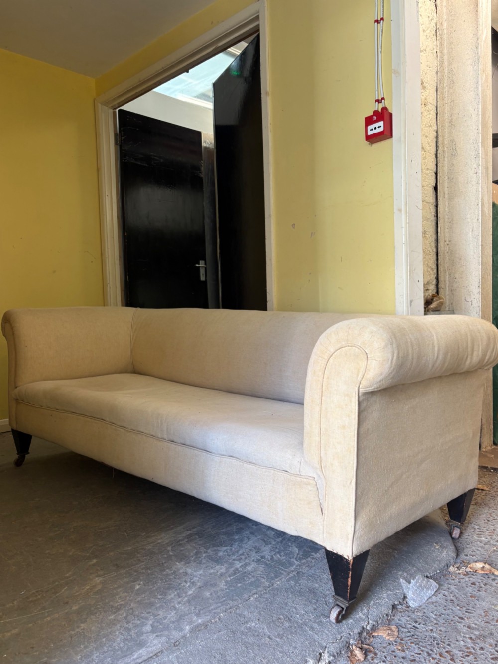 A large 19th-century Victorian Chesterfield sofa upholstered in cream calico linen featuring deep rolled arms and tapered dark timber legs with brass castors. View V