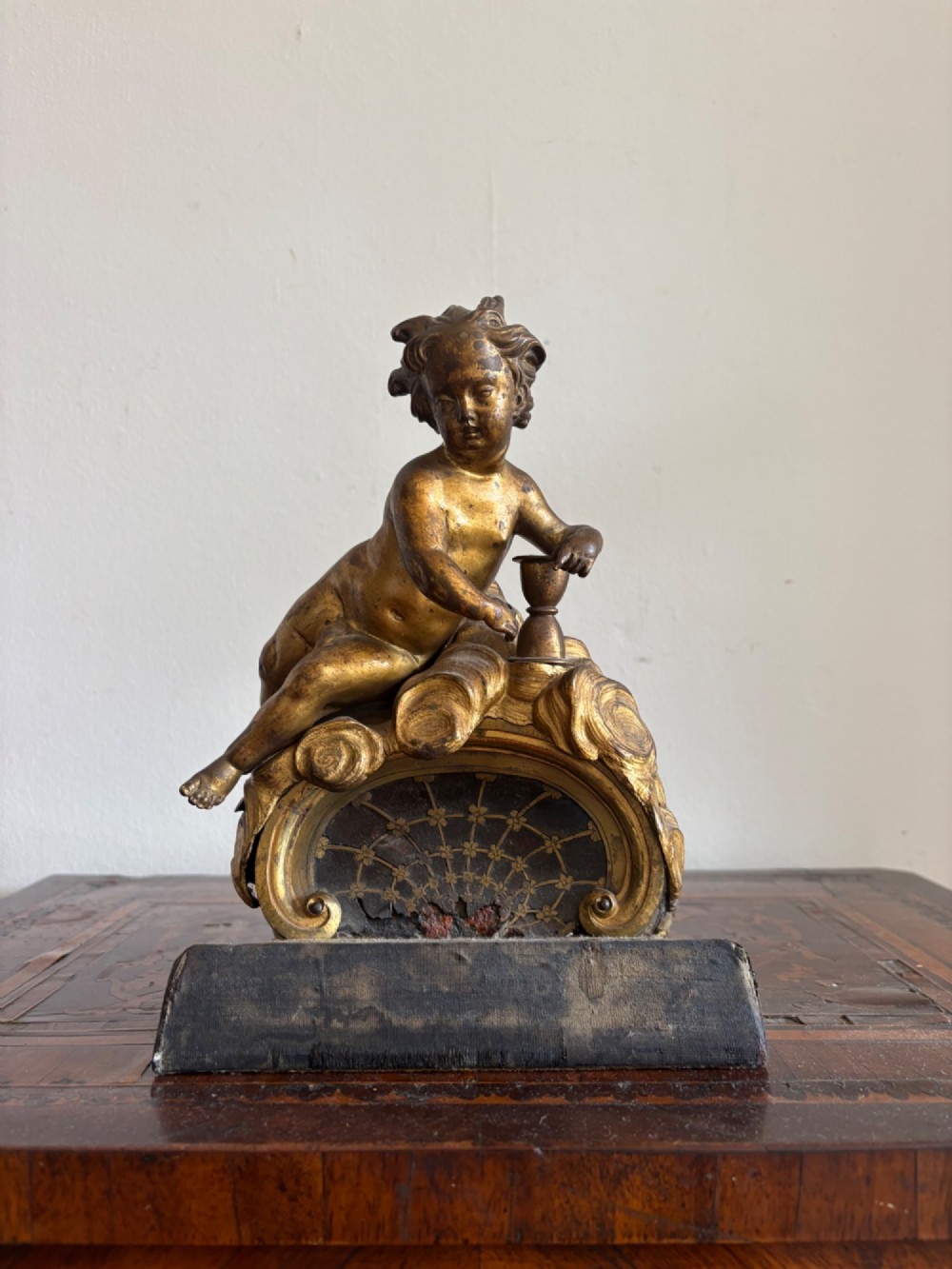 A late eighteenth or nineteenth-century French gilt bronze ormolu sculpture featuring a reclining putto holding a small vessel above a scrolled arch base. View IV